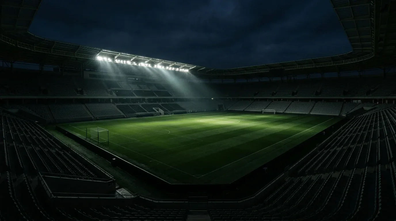Fodboldstadion med tomme tribuner og en enkelt spotlyskegle over banen efter en afsluttet turnering