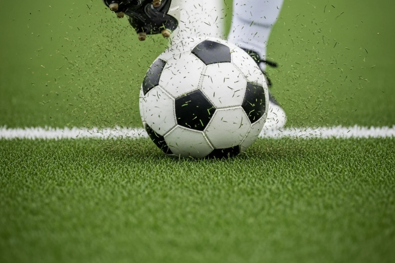 Nærbillede af en fodboldspillers fødder der sparker bolden på en grøn græsbane